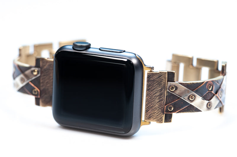 Narrow Juggler Apple Watch band with ribbons of copper and silver hand-riveted to the band in a criss-cross pattern. Watch faces left.