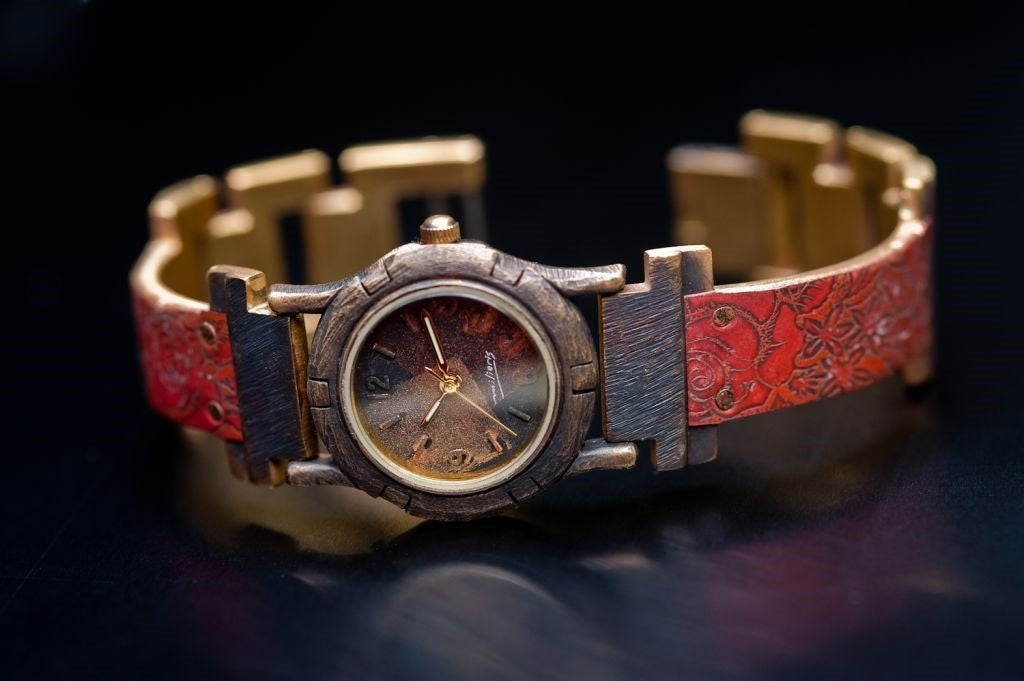 The Gardel features a small, hand-painted watch face, with a narrow red copper watch band engraved with a unique floral design.
