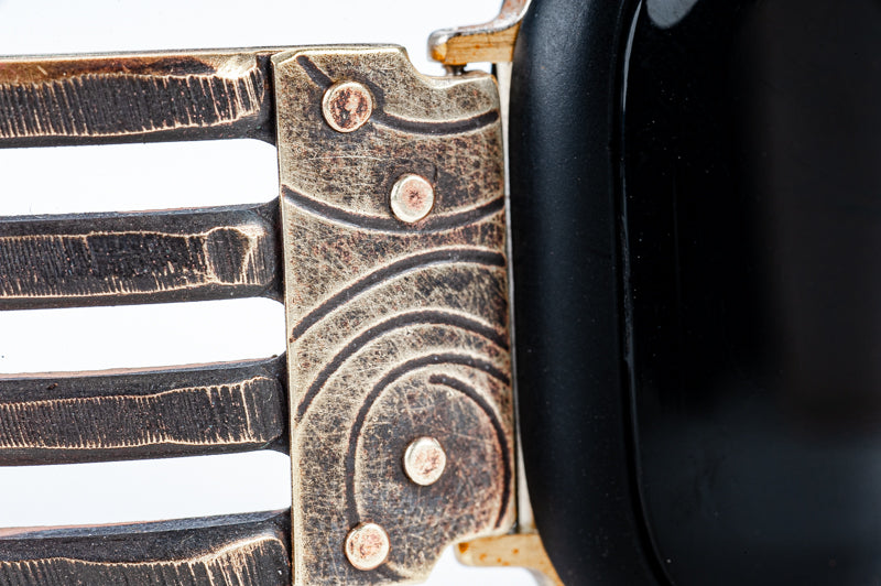 Close up of the metalwork on the Jaffa Bridge Apple watch band. Brass trim embossed with spirals is riveted to a forked brass band.