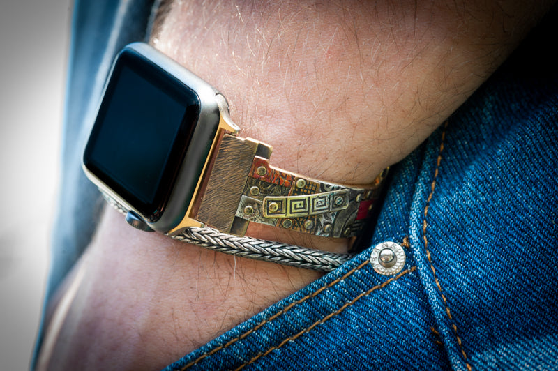 The Golan Apple Watch band on a man's wrist. The narrow band is hand-riveted with a mosaic of silver, copper and brass. A truly unique design. 